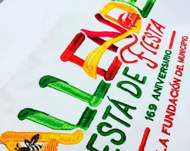 Bordado a varios colores sobre tela blanca con el texto «Fiesta de Fiestas» y «169 aniversario de la fundación del municipio».