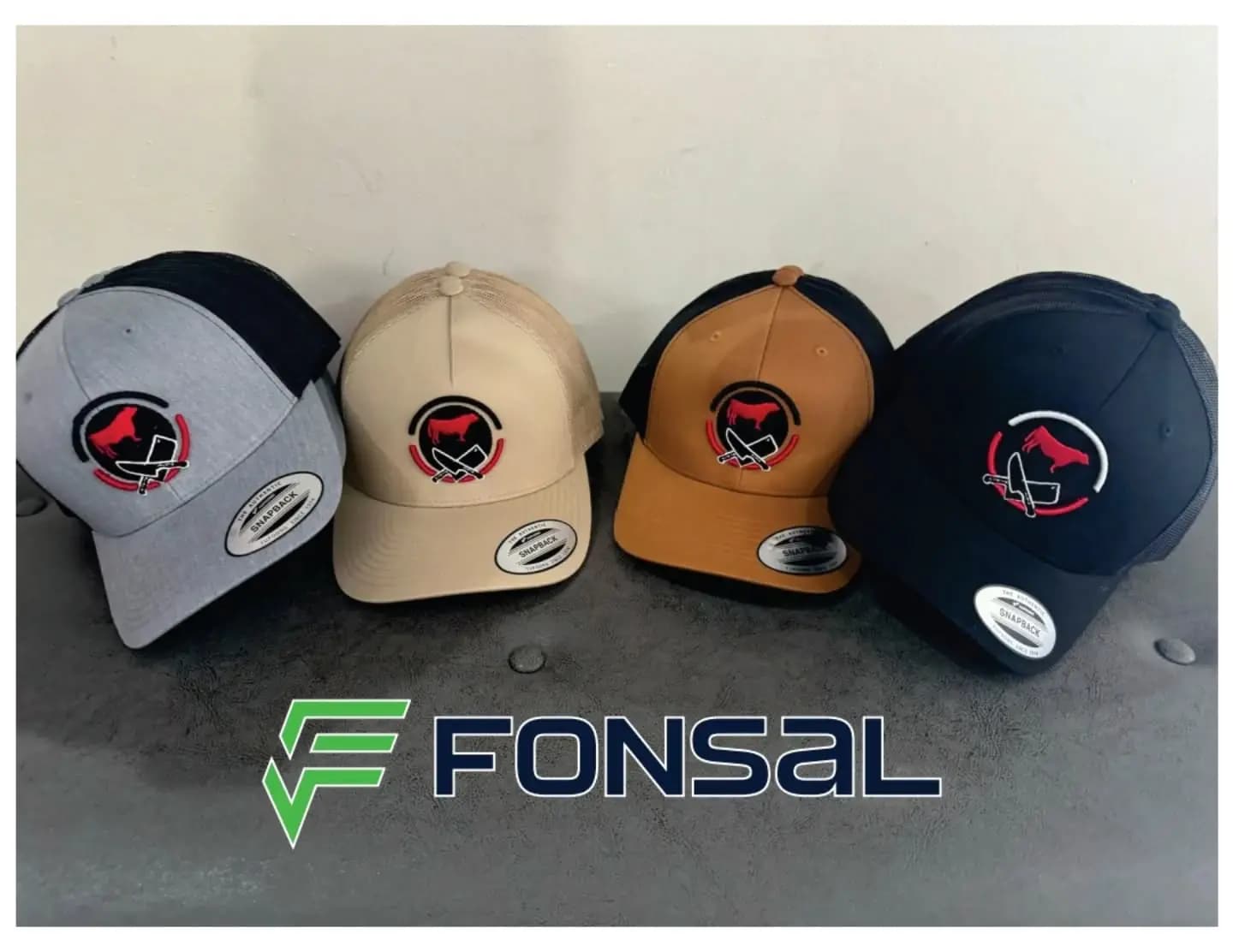 Cuatro gorras tipo snapback en gris, beige, camel y azul marino, cada una con el mismo logotipo bordado de un toro rojo y dos cuchillos cruzados.