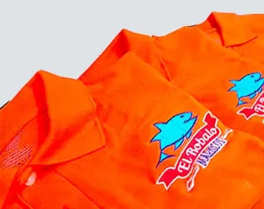 Varios polos naranjas apilados, cada uno con el logotipo bordado de un restaurante de mariscos: un pez azul sobre una cinta roja.